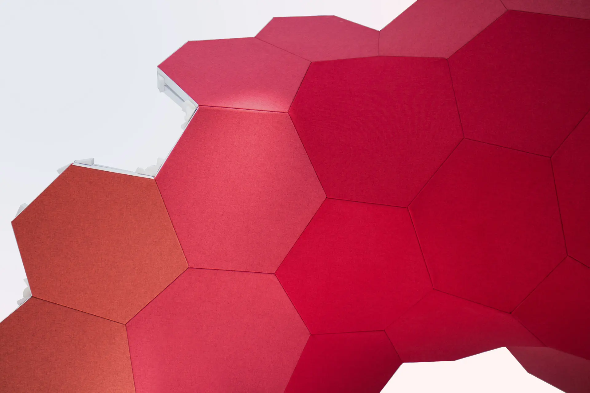 A close-up of interlocking hexagonal panels in shades of red and orange, forming a modern, geometric surface against a light background.