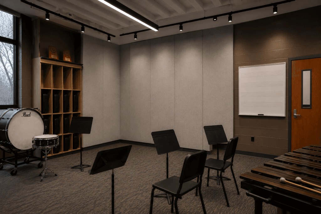 A music classroom with percussion instruments, including a bass drum and xylophone, three music stands with chairs, a wall-mounted whiteboard with musical staff lines, and shelves holding black cases near a window.