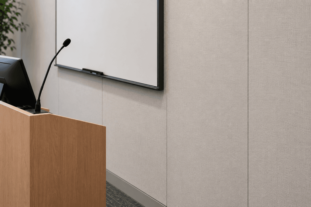 A wooden podium with a microphone and computer monitor stands in front of a blank whiteboard in a modern, neutral-toned conference room.