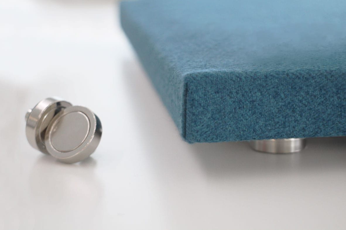 A close-up of a metal disc and a corner of a blue upholstered panel with metal feet, both resting on a white surface.