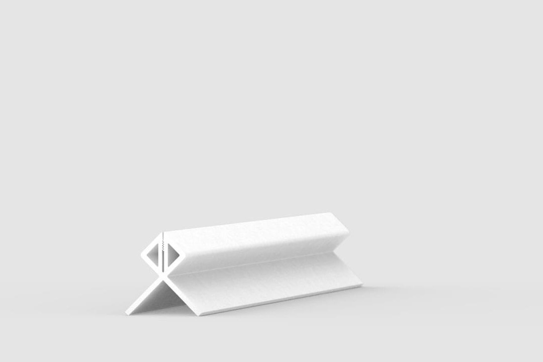 A white geometric object with triangular and diamond-shaped cutouts sits on a light gray surface against a plain, light gray background.