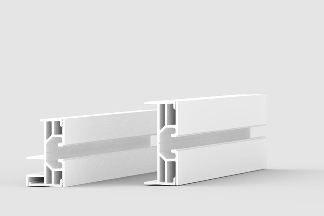 Two white aluminum extrusion profiles are placed on a light gray surface. The profiles have a rectangular shape with grooves and channels visible on their inner sides, suggesting use in construction or framing.